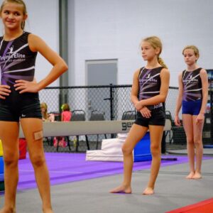 3 gymnasts standing on the mat during gymnastics class.