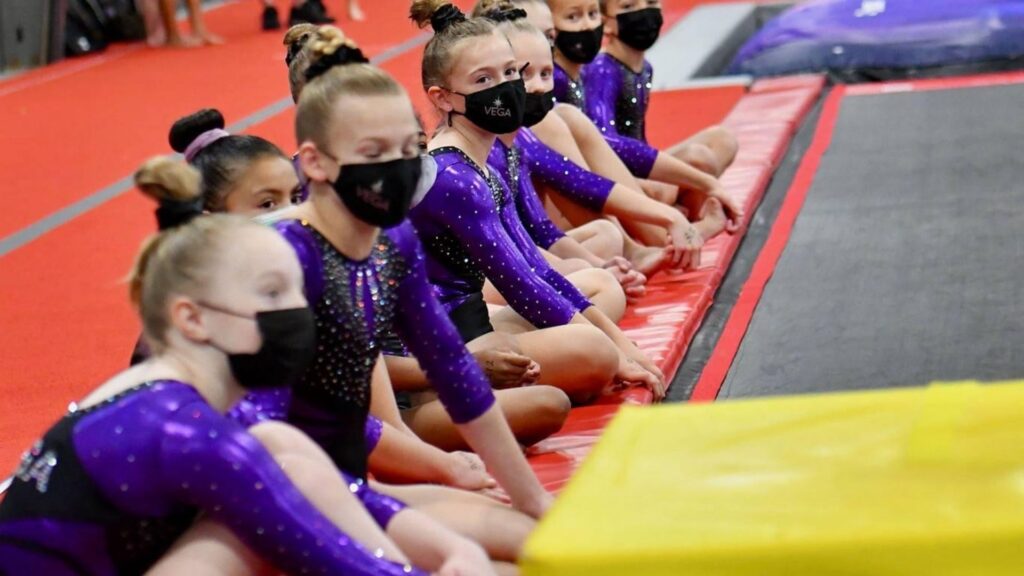 A group of gymnasts sitting on a mat waiting to compete.