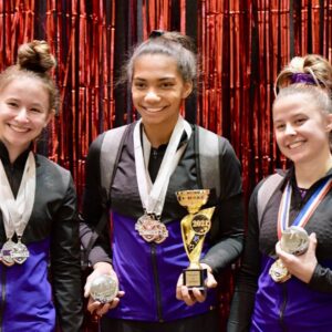 three female gymnasts pose with trophies and medals