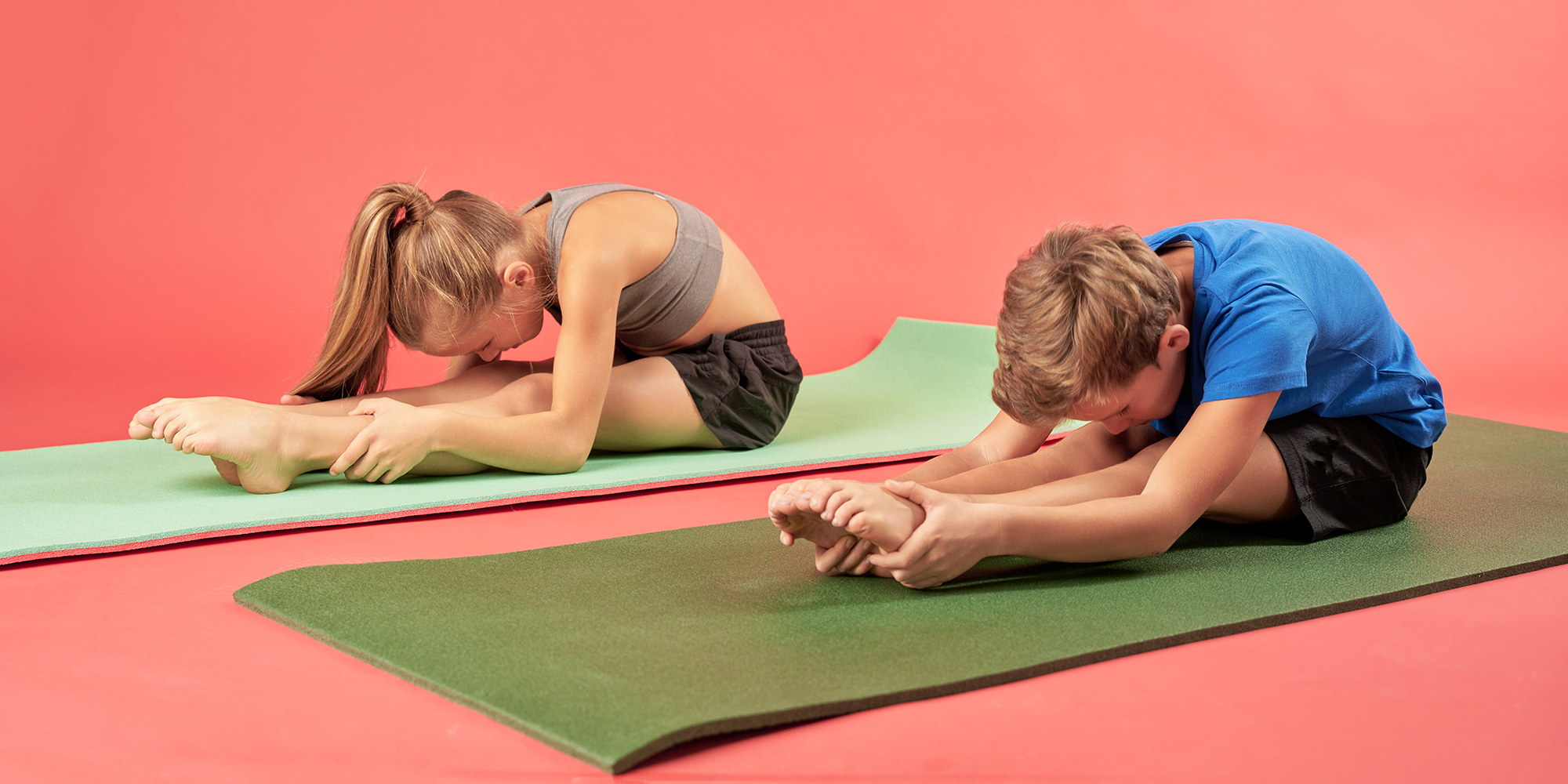 Cute kids in sportswear sitting on yoga mats and doing seated forward bend pose or Paschimottanasana