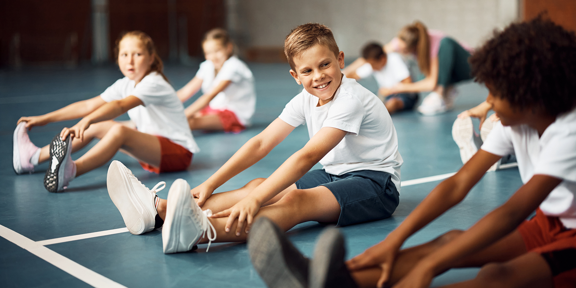Happy schoolboy talks to his friend while doing stretching exercises on PE class.